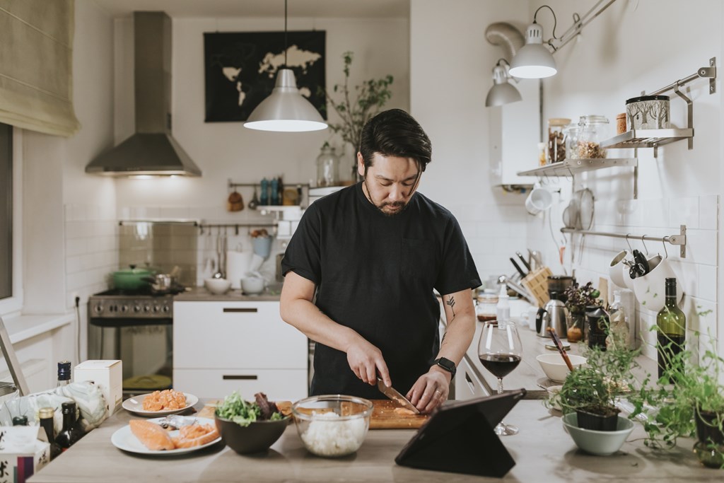 A man is cutting vegetables on a cutting board in a kitchen.