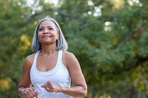A woman in a white tank top is running outdoors.