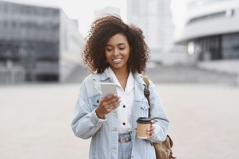 A woman with curly hair is holding a cup and looking at her phone.