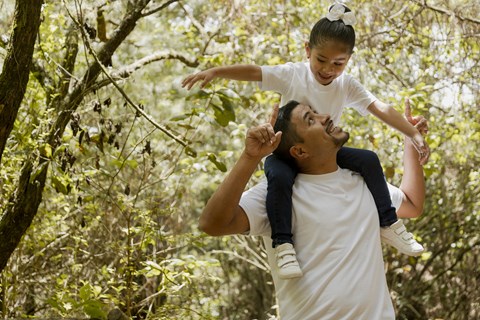 A man lifts a child into the air in a forest.