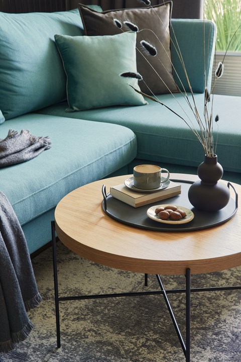 A living room with a blue couch and a wooden coffee table with a vase, book, and cup on it.