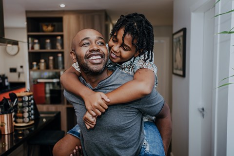 A man is giving a piggyback ride to a young girl in a kitchen.