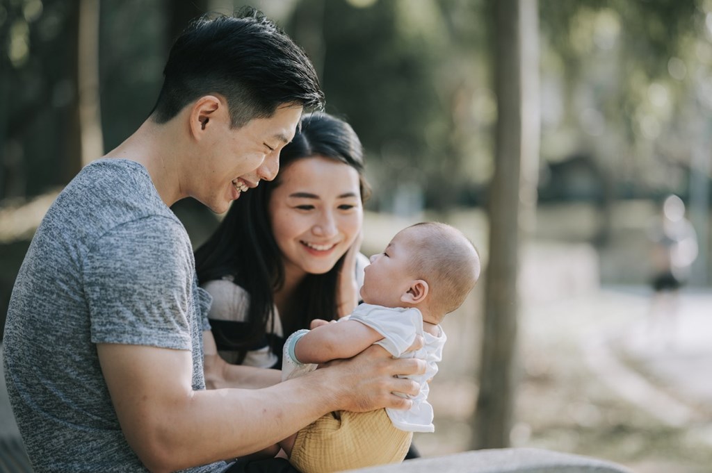 A man and woman holding a baby in a park.
