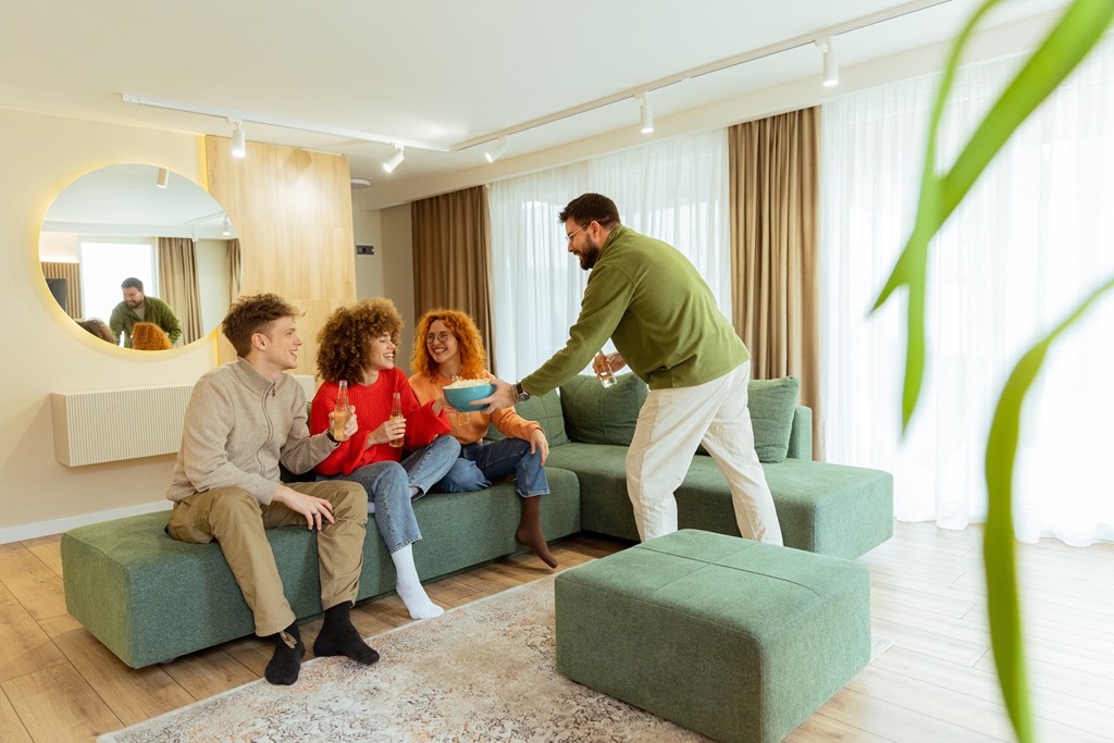 A man serving food to two people sitting on a green couch in a living room.