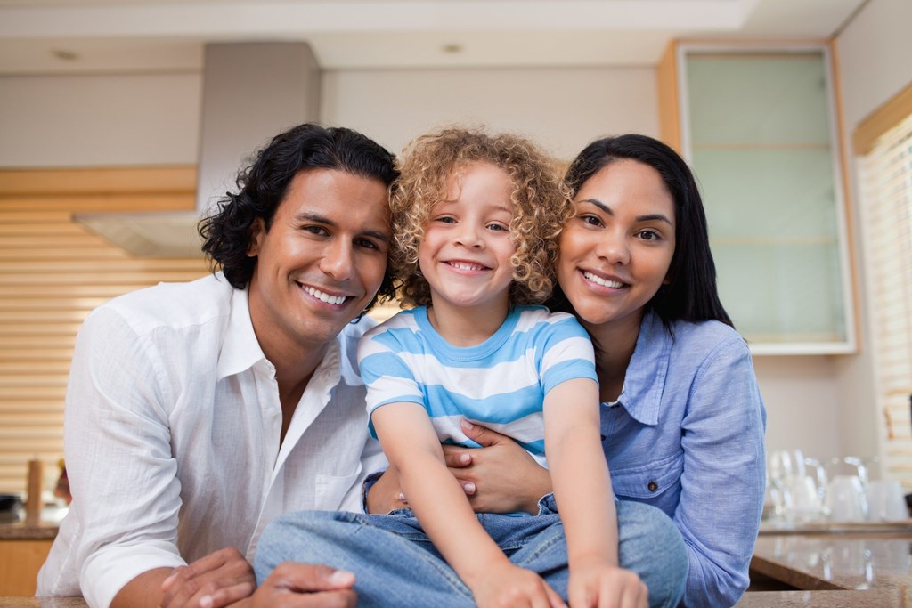 A family of three is sitting together in a kitchen.