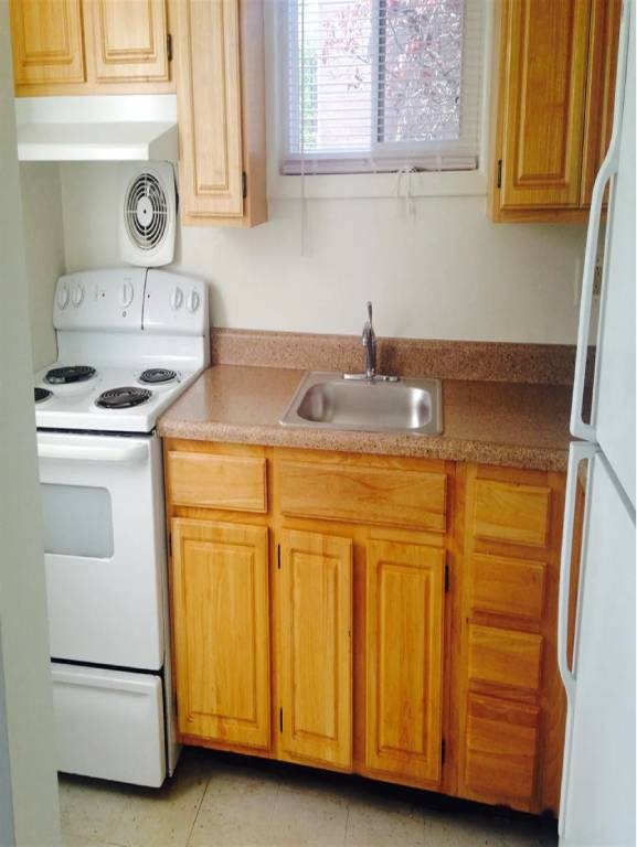A white stove and sink in a kitchen with wooden cabinets.