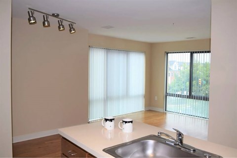 A kitchen with a sink, a window with blinds, and a white countertop.