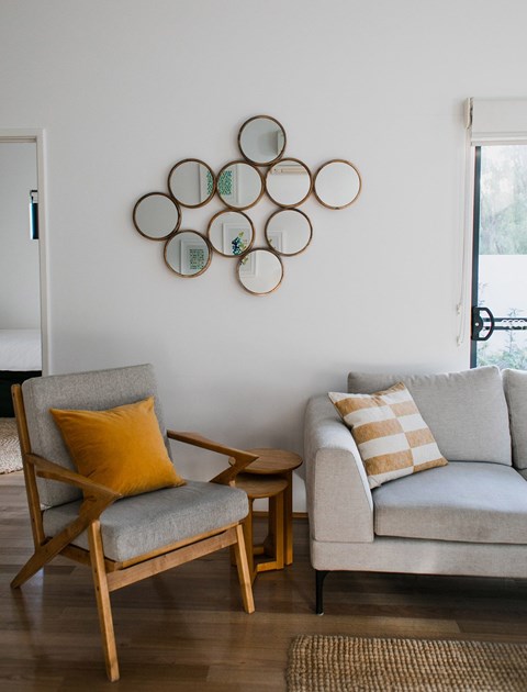 A living room with a grey couch, a wooden chair and a wall decoration.