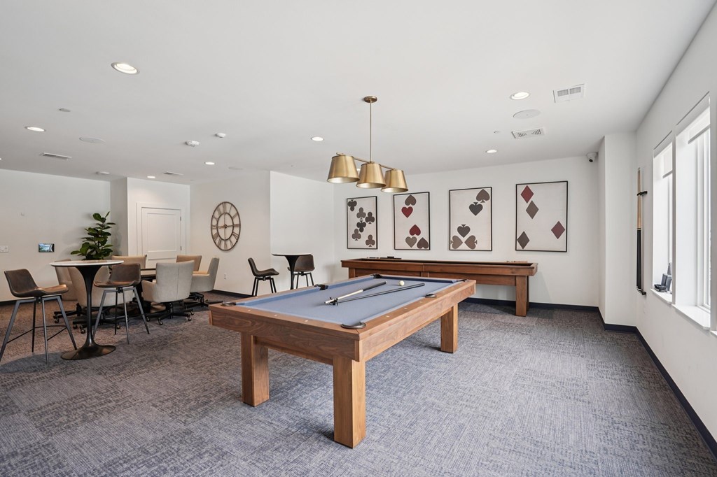 A pool table is in the middle of a room with a carpet and a few chairs.
