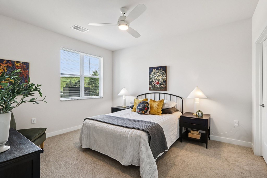 A bedroom with a bed, nightstand, and a plant.