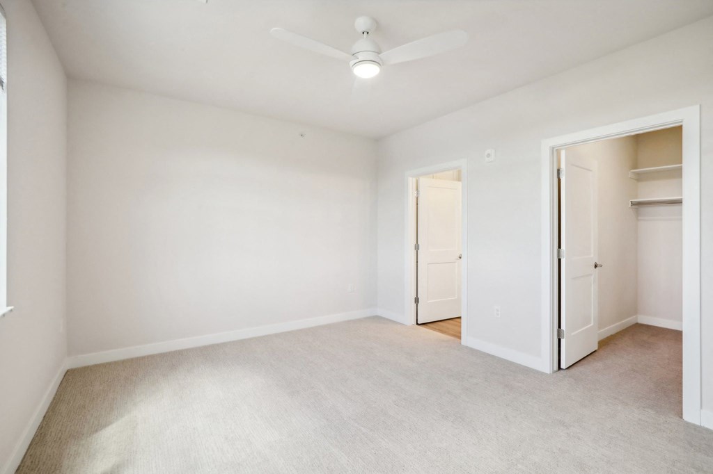an empty living room with white walls and a ceiling fan