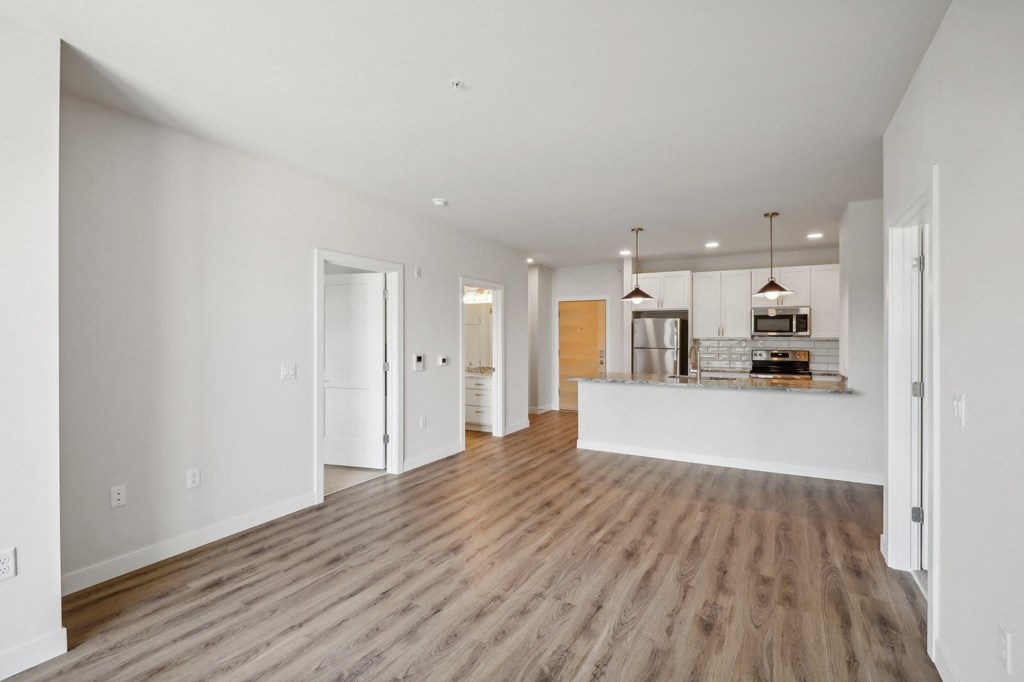 a living room and kitchen with white walls and wood floors