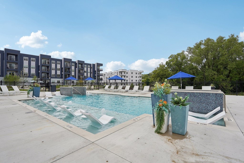 A pool area with a blue umbrella and two vases with flowers.