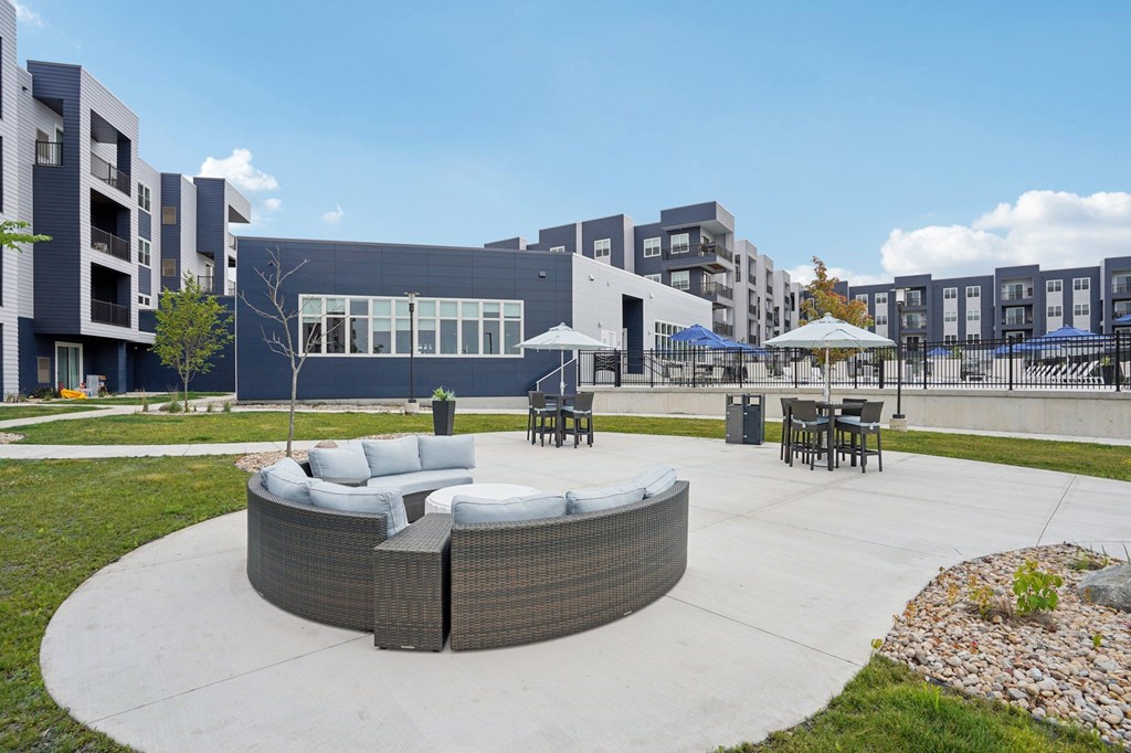 A modern outdoor seating area with a circular sofa and chairs is surrounded by a concrete patio and a grassy area.