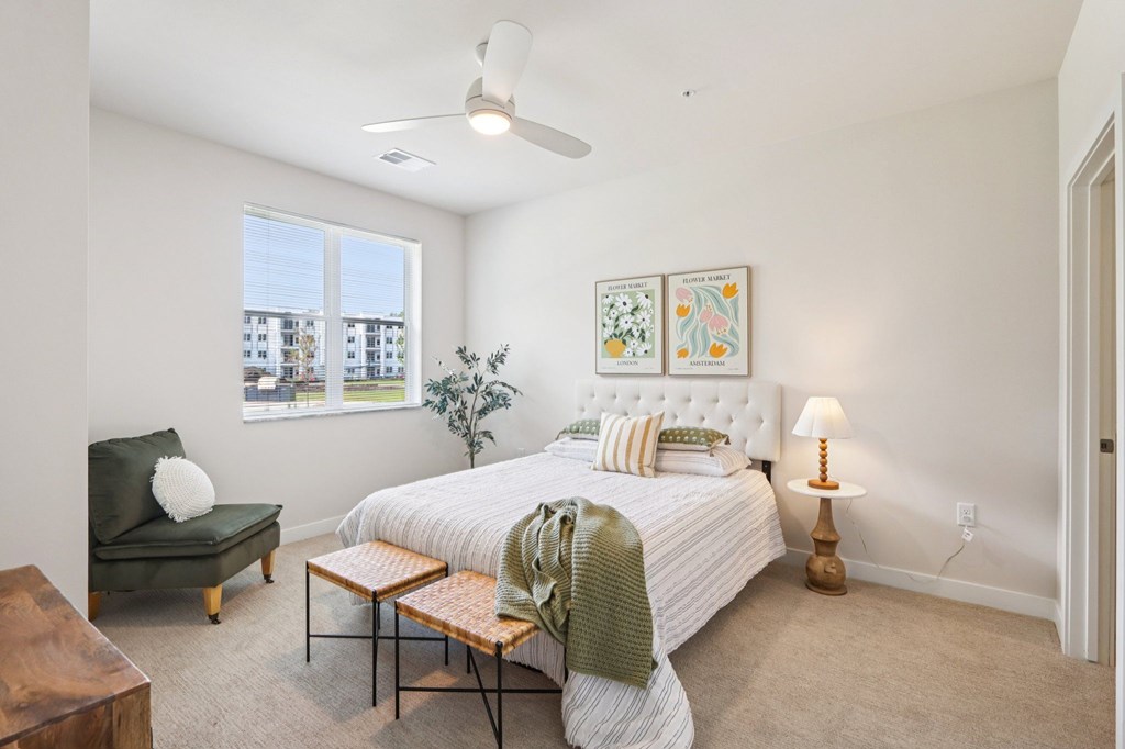 A bedroom with a large bed, a green chair, and a ceiling fan.