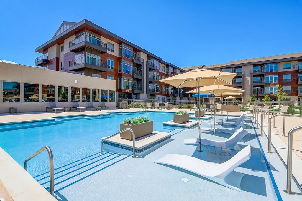 a swimming pool with lounge chairs and umbrellas in front of a hotel