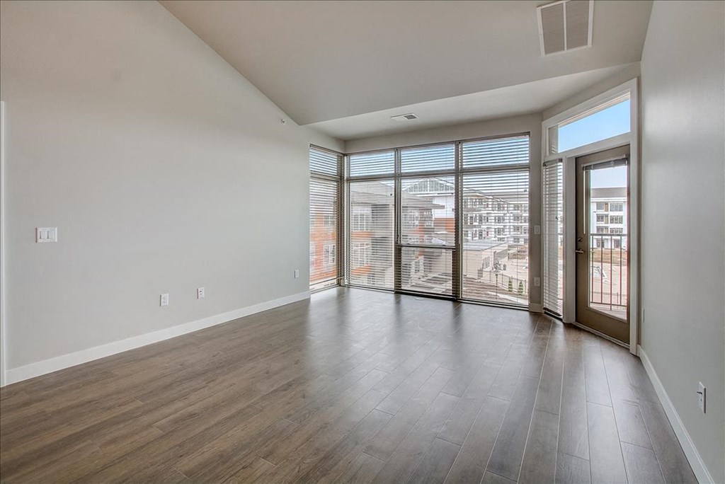 an empty living room with a large window and a door to a balcony