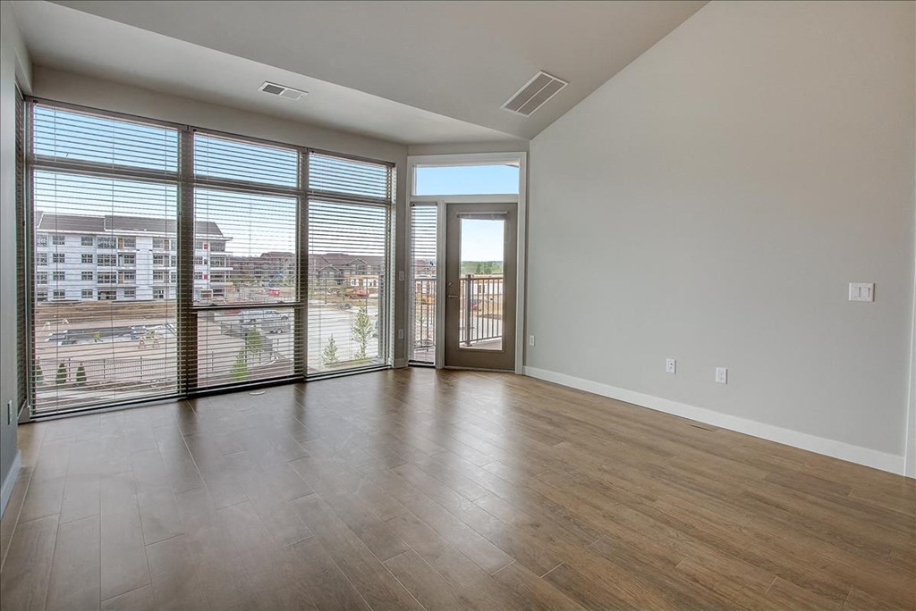 an empty living room with large windows and a door to a balcony