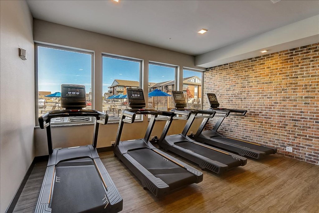 a gym with a row of cardio machines and a brick wall