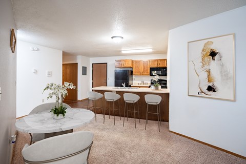 A white marble table with a vase of white flowers on it sits in a kitchen with a bar area.