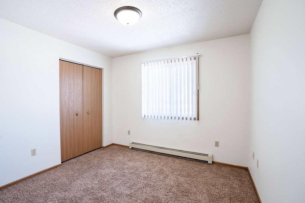 A room with a brown carpet and a window with blinds.