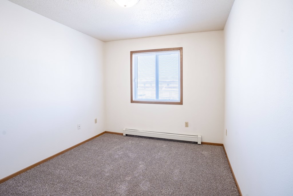 A room with a window and a carpeted floor. Fargo, ND Country Edge Apartments