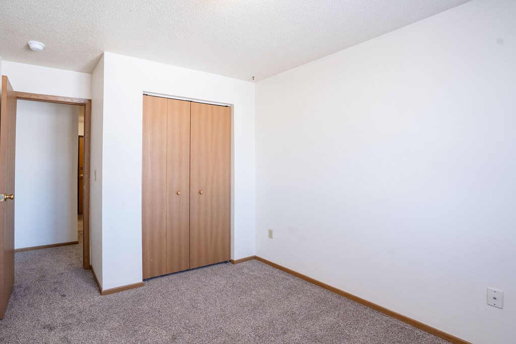 A room with a brown door and carpeted floor. Fargo, ND Country Edge Apartments