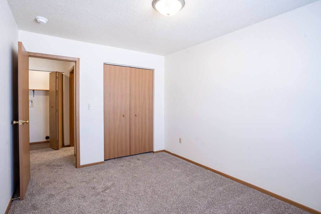 A room with a carpeted floor and a closet. Fargo, ND Country Edge Apartments