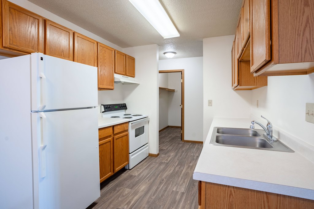 A kitchen with a white refrigerator, wooden cabinets, and a sink. Fargo, ND Country Edge Apartments
