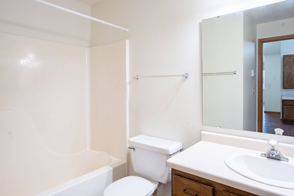 A white toilet sits next to a white sink in a bathroom. Fargo, ND Somerset Apartments