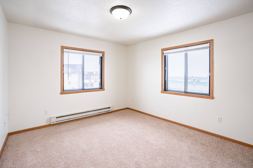 A room with two windows and a carpeted floor. Fargo, ND Somerset Apartments