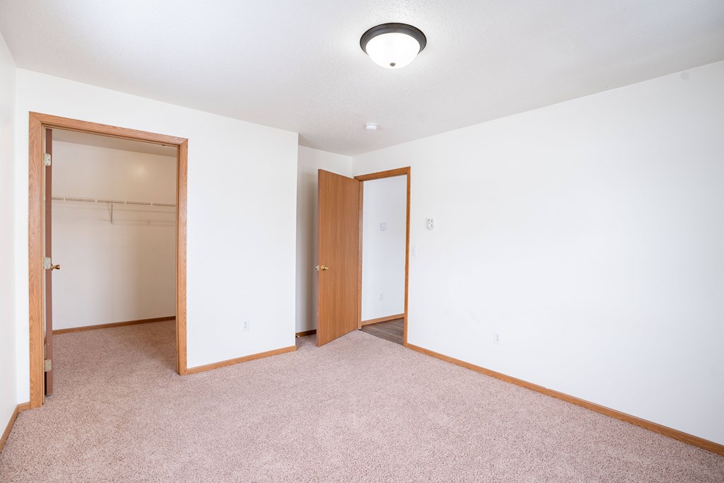 A bedroom with a carpeted floor and a walk in closet. Fargo, ND Somerset Apartments