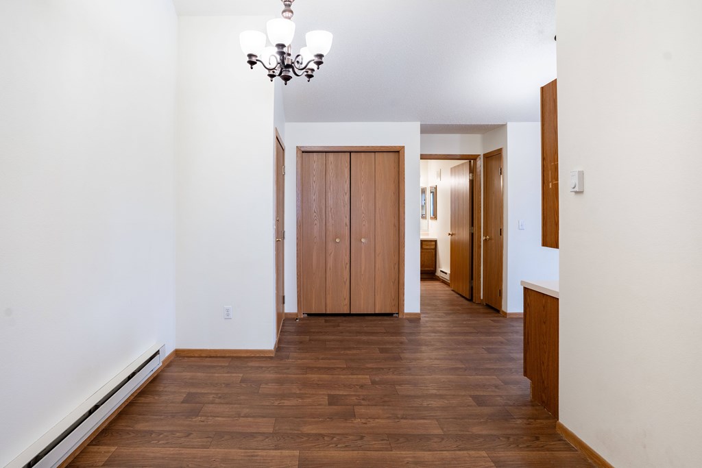A hallway with a chandelier and a wooden floor. Fargo, ND Somerset Apartments