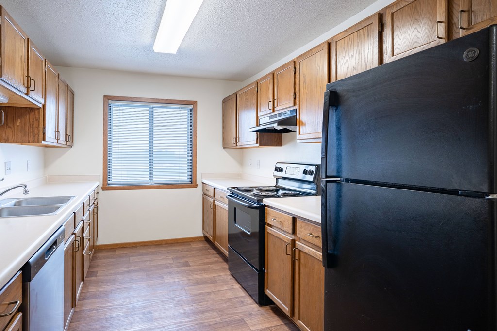 A kitchen with wooden cabinets and a black refrigerator. Fargo, ND Somerset Apartments