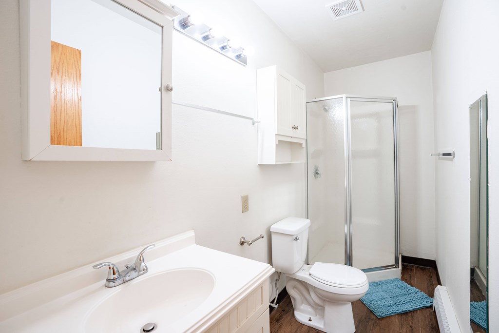 A white sink with a silver faucet is on the left side of a white toilet in a bathroom. Fargo, ND L&R Apartments