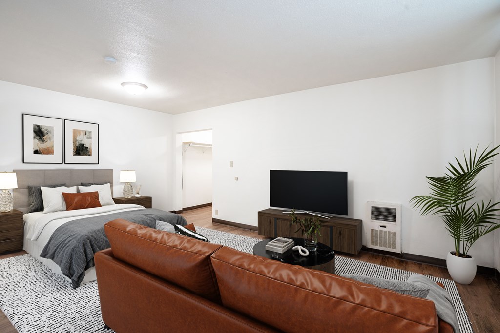 A brown leather couch sits in a living room with a television and a bed in the background. Fargo ND, L&R Apartments