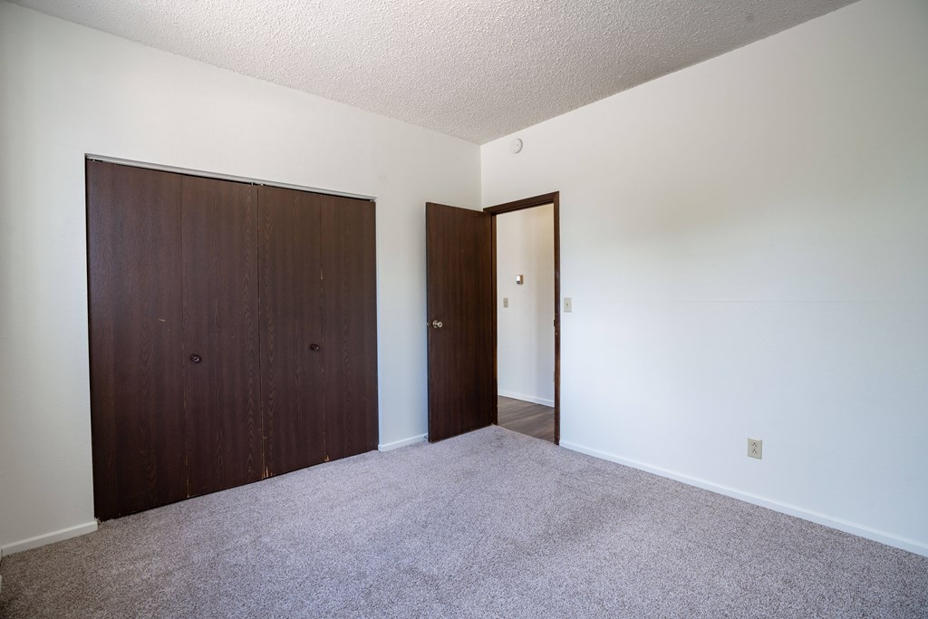 A room with a carpeted floor and two doors. Bismarck, ND Belmont Apartments