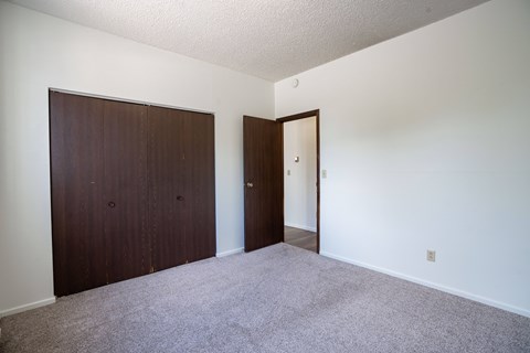 A room with a carpeted floor and two doors. Bismarck, ND Belmont Apartments