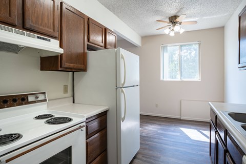A kitchen with a white refrigerator, white stove, and wooden cabinets. Bismarck, ND Belmont Apartments