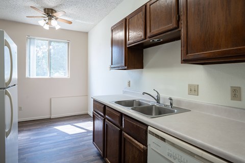 A kitchen with wooden cabinets and a white dishwasher. Bismarck, ND Belmont Apartments
