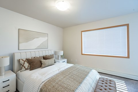 A bedroom with a large bed and a painting on the wall. Moorhead, MN Sandy Creek Apartments
