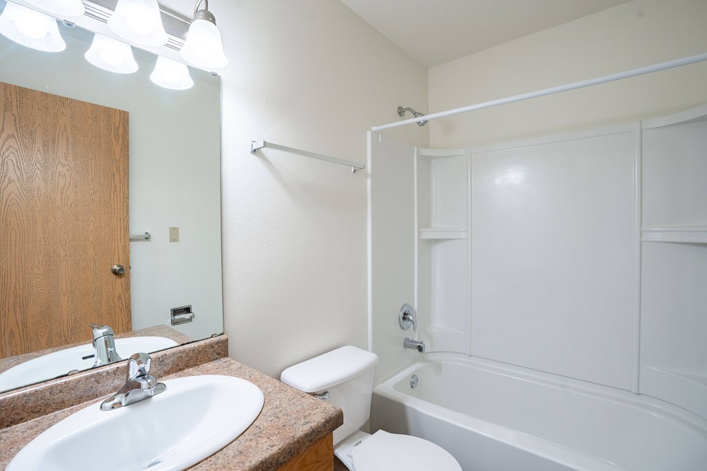 A white bathroom with a toilet, sink, and bathtub. West Fargo, ND Saddlebrook Apartments