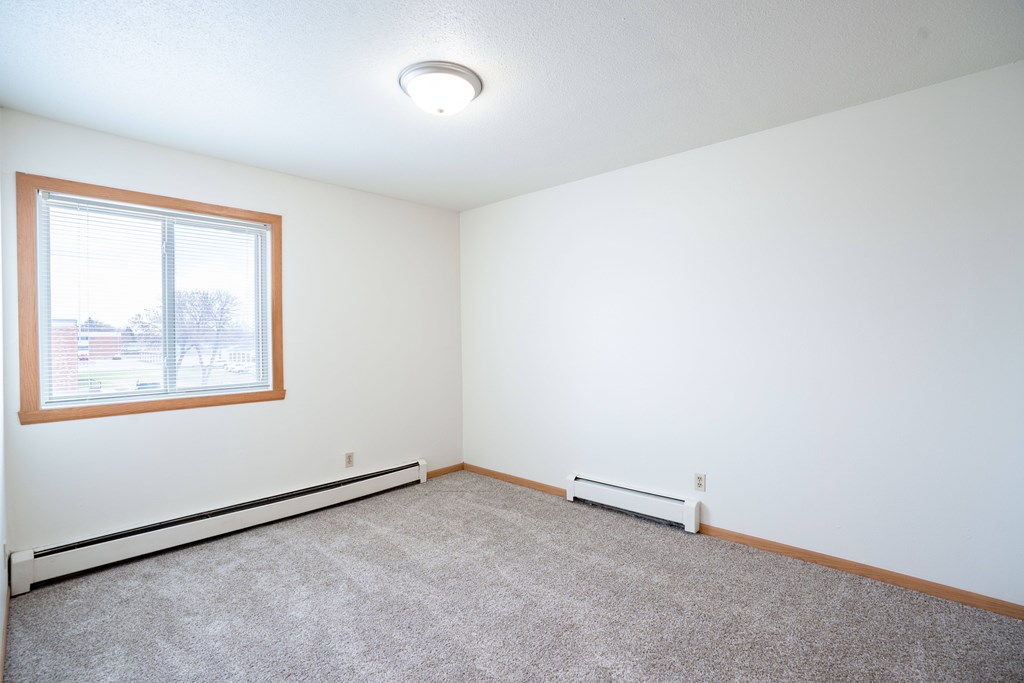 A room with a window and carpeted floor. West Fargo, ND Saddlebrook Apartments