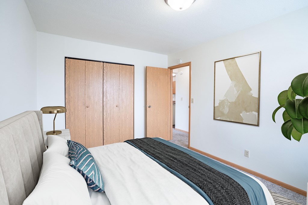 A bedroom with a bed, a lamp, and a painting on the wall. West Fargo, ND Saddlebrook Apartments