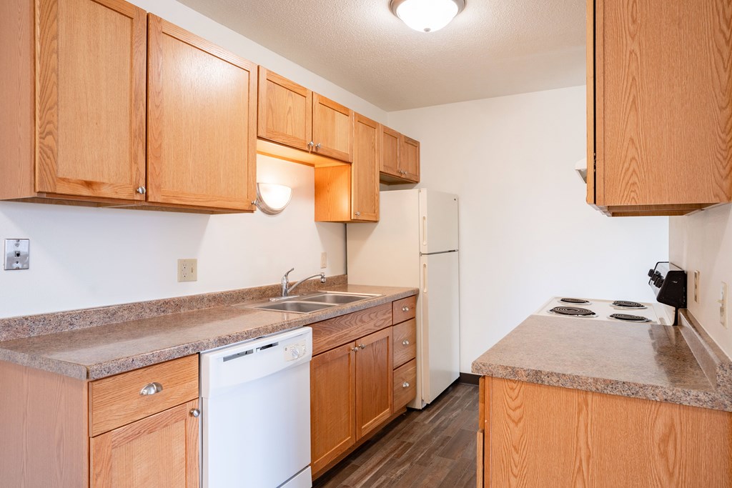A kitchen with wooden cabinets and a white dishwasher. West Fargo, ND Saddlebrook Apartments