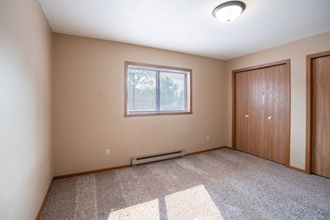 A room with a window, carpet, and two doors.