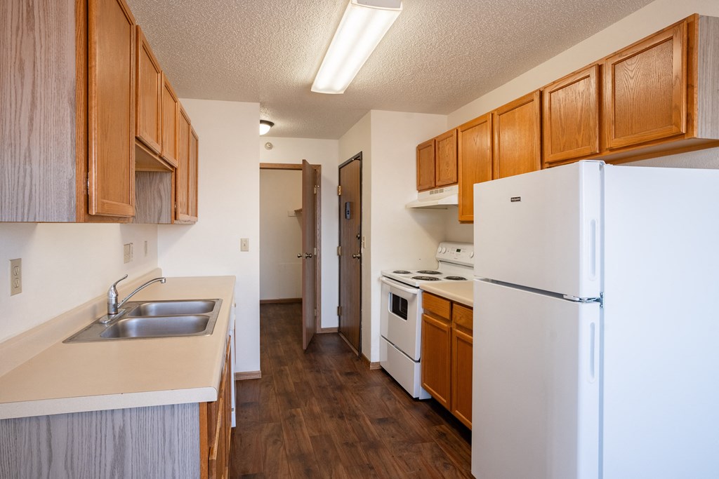 A kitchen with a white refrigerator, sink, and wooden cabinets. Fargo, ND Fieldstone Apartments