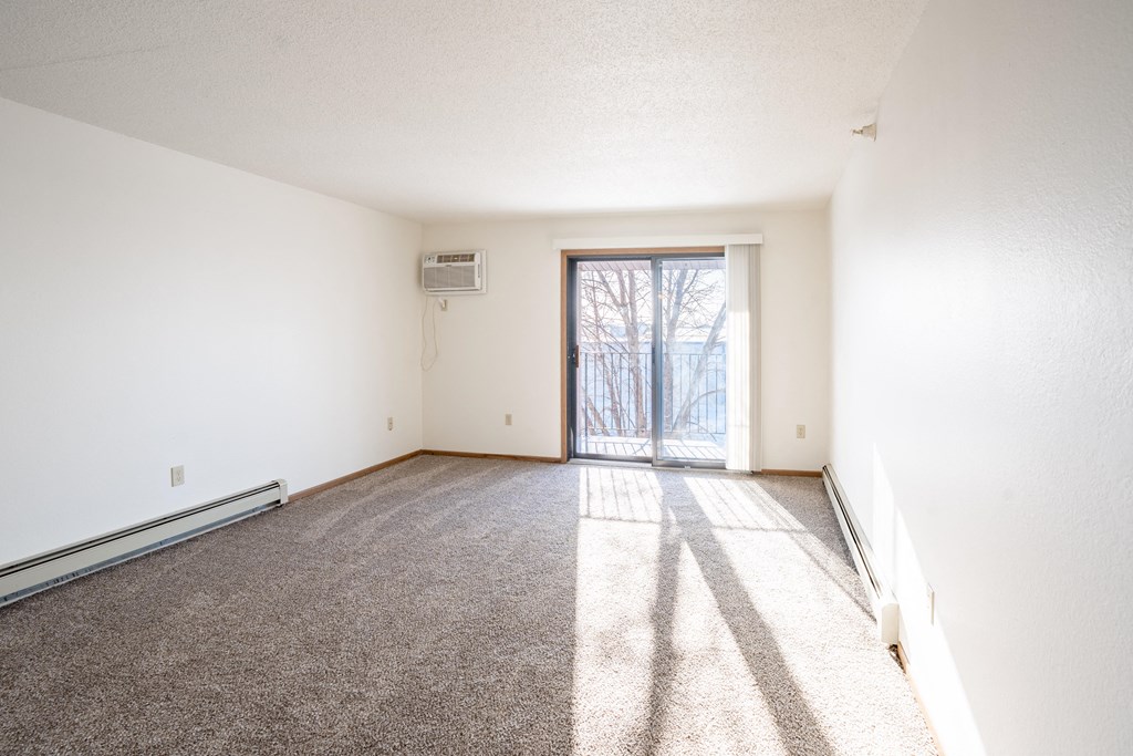 A room with a carpeted floor and a sliding glass door leading outside. Fargo, ND Fieldstone Apartments