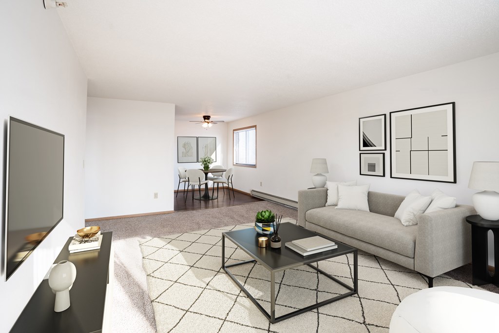 A living room with a grey couch, a black coffee table, and a television on the left side. Fargo, ND Fieldstone Apartments