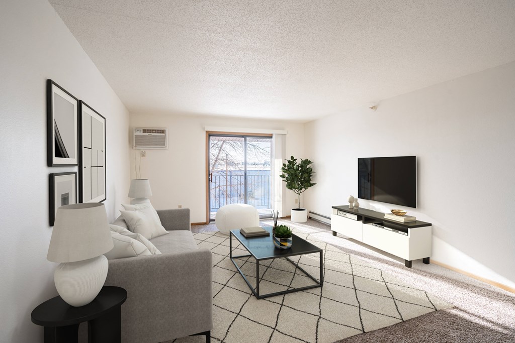 A living room with a grey couch, a black and white coffee table, a white television, and a plant. Fargo, ND Fieldstone Apartments
